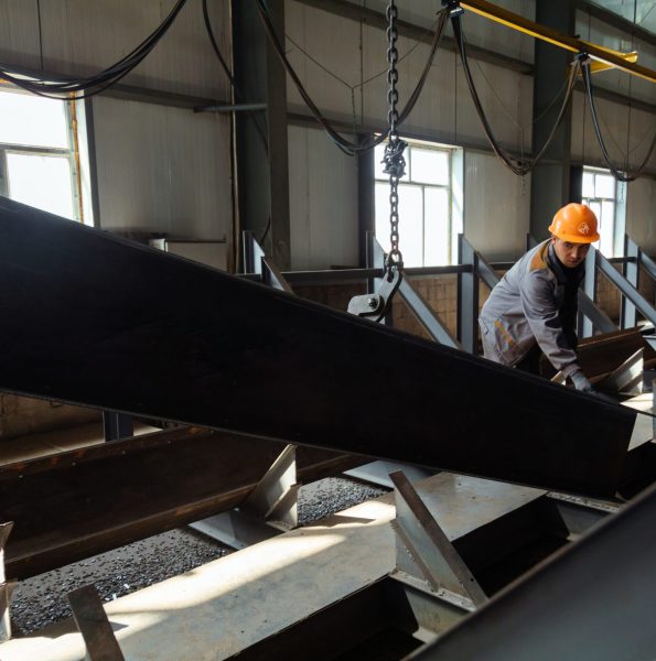 Worker in helmet receiving a metal profiles from crane in warehouse